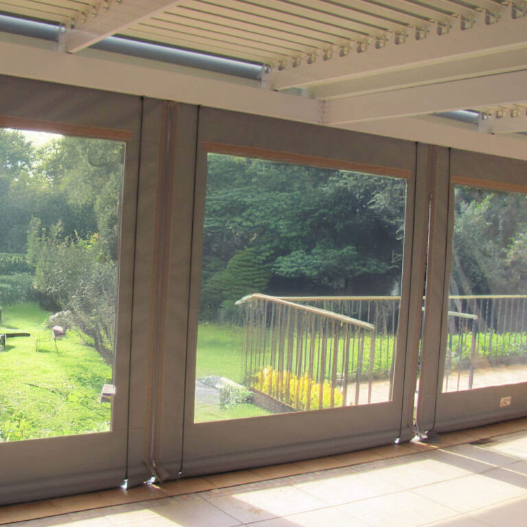 Inside a patio enclosed by zipped blinds with full-width clear panels onto a garden