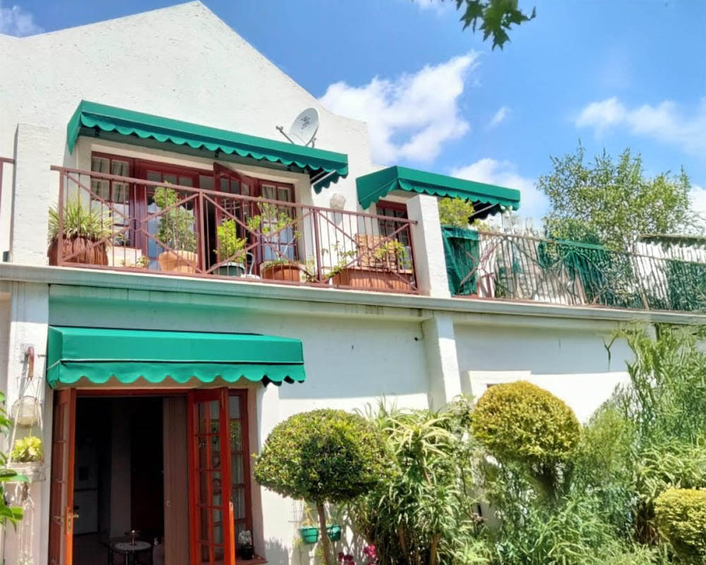 Green scalloped canvas awnings over the doors and balcony of a white double-storey home