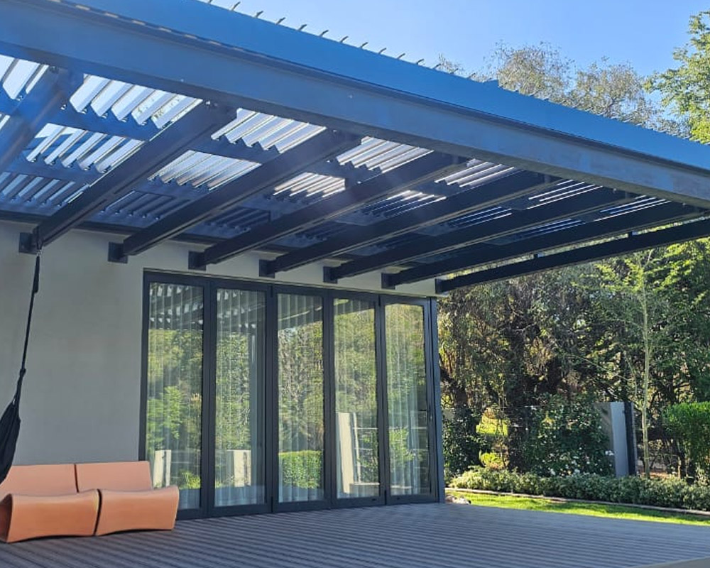Charcoal steel pergola with a clear roof over a timber deck beside folding glass doors