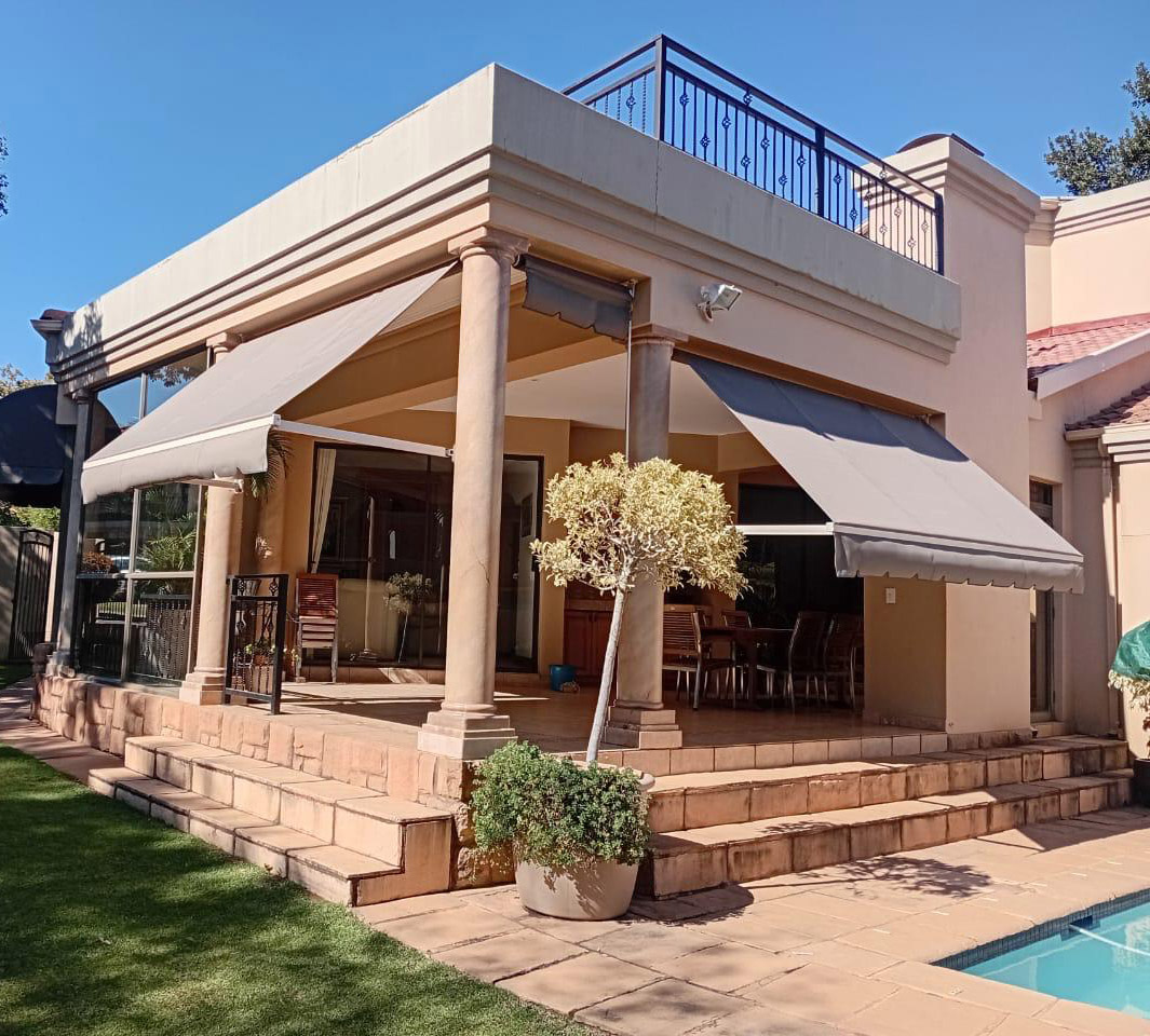 Pair of grey drop-arm awnings angled out over a columned patio beside a pool