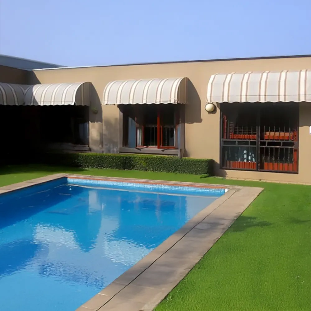 Row of cream striped pram awnings along a house overlooking a swimming pool