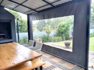 Charcoal patio blind with a large clear PVC window enclosing a covered braai patio and dining area