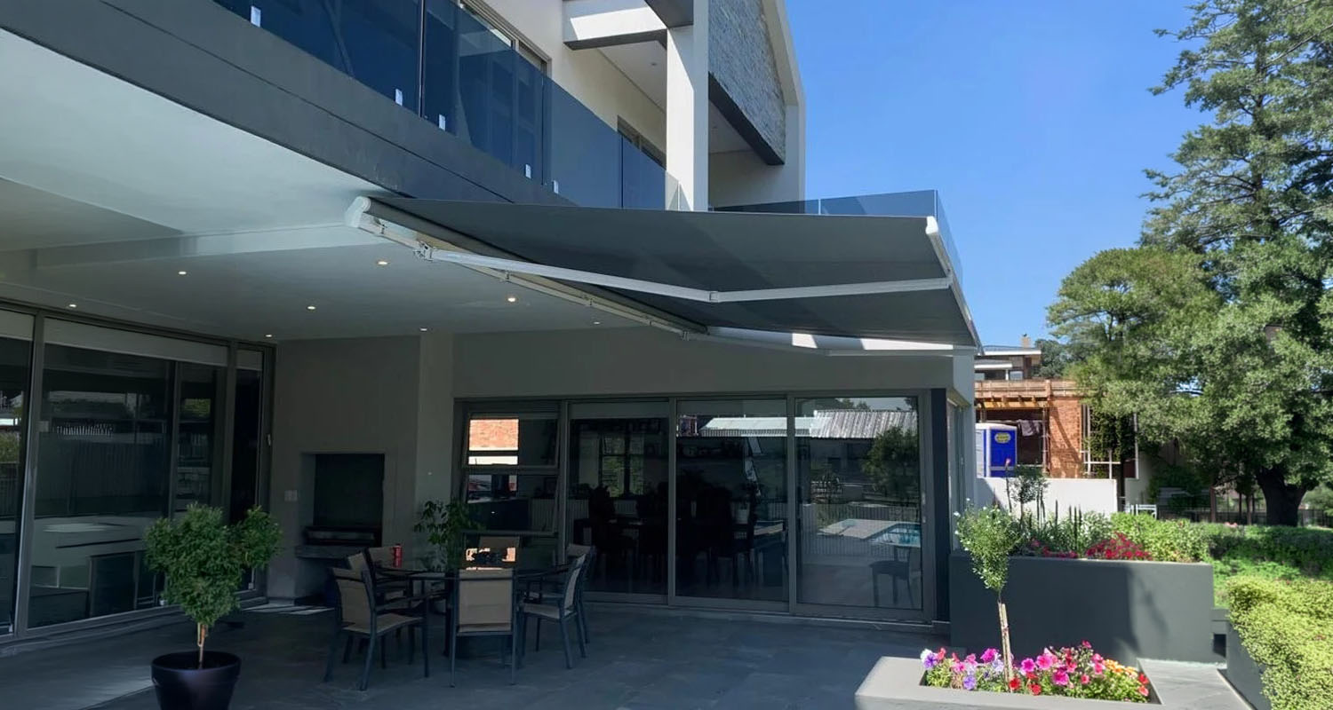 Grey retractable fold-arm awning extended over a patio, made and fitted by Patio SA